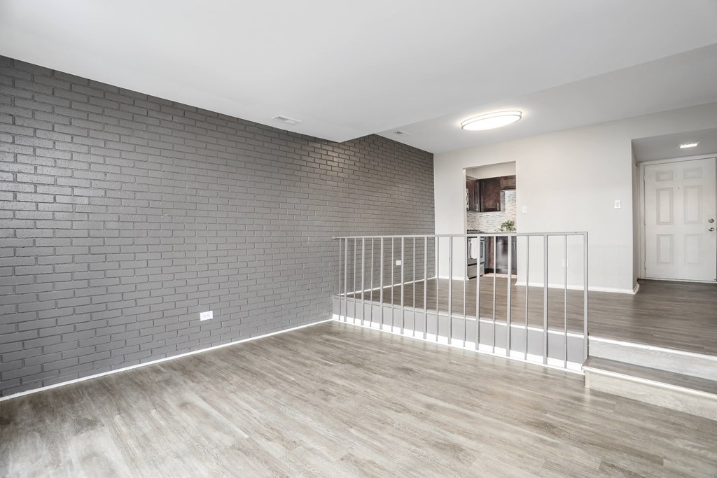 an empty living room with a staircase and a brick wall