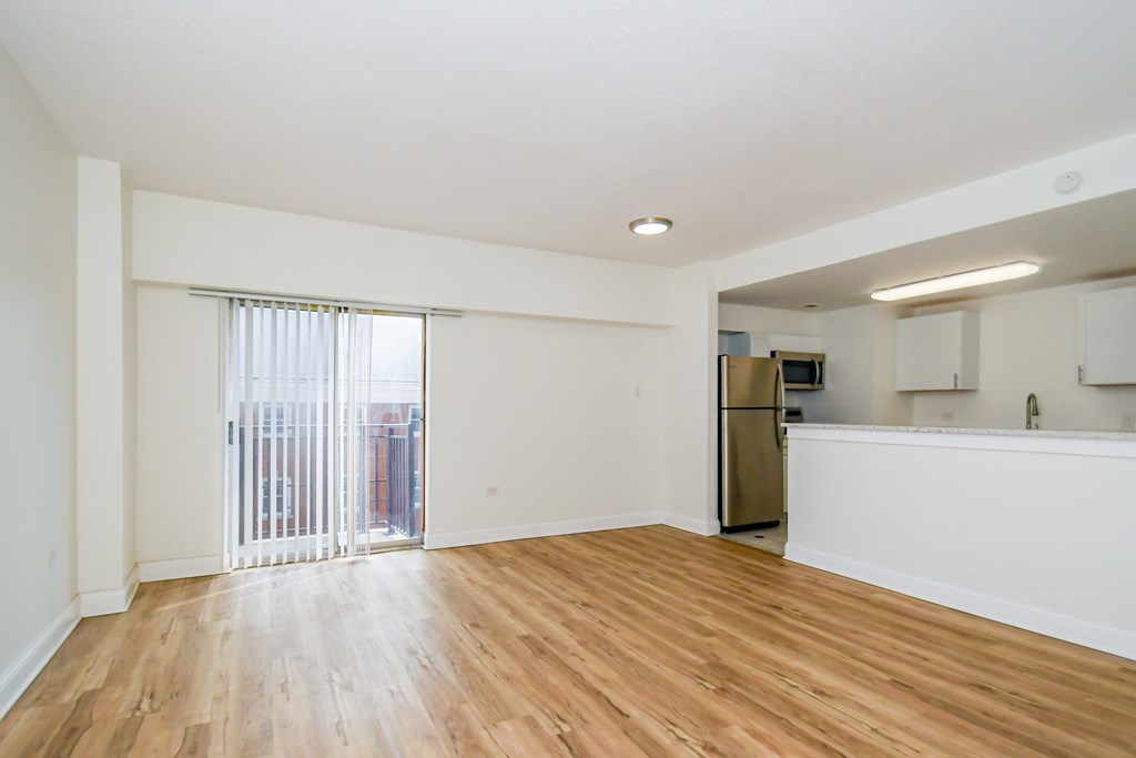 A spacious room with wooden floors and a refrigerator in the corner.