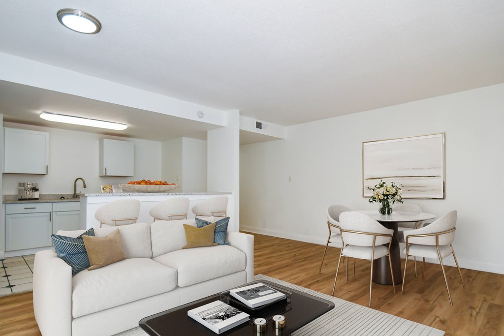 A white couch with blue pillows sits in a living room with a dining table and chairs.