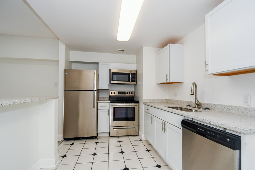 A kitchen with white cabinets and black and white tiled flooring.