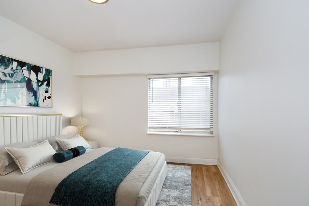 A bedroom with a bed, pillows, a blanket, a lamp, and a window with blinds.