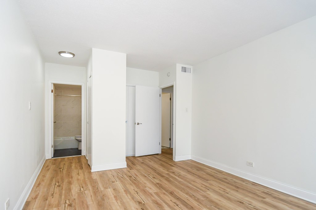 A room with white walls and wooden flooring with three doors.