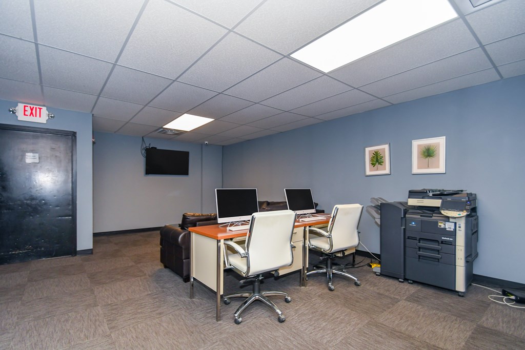 A room with a desk, chairs, and computers.