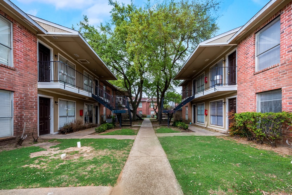 A tree in front of a brick building with a pathway leading to the entrance.