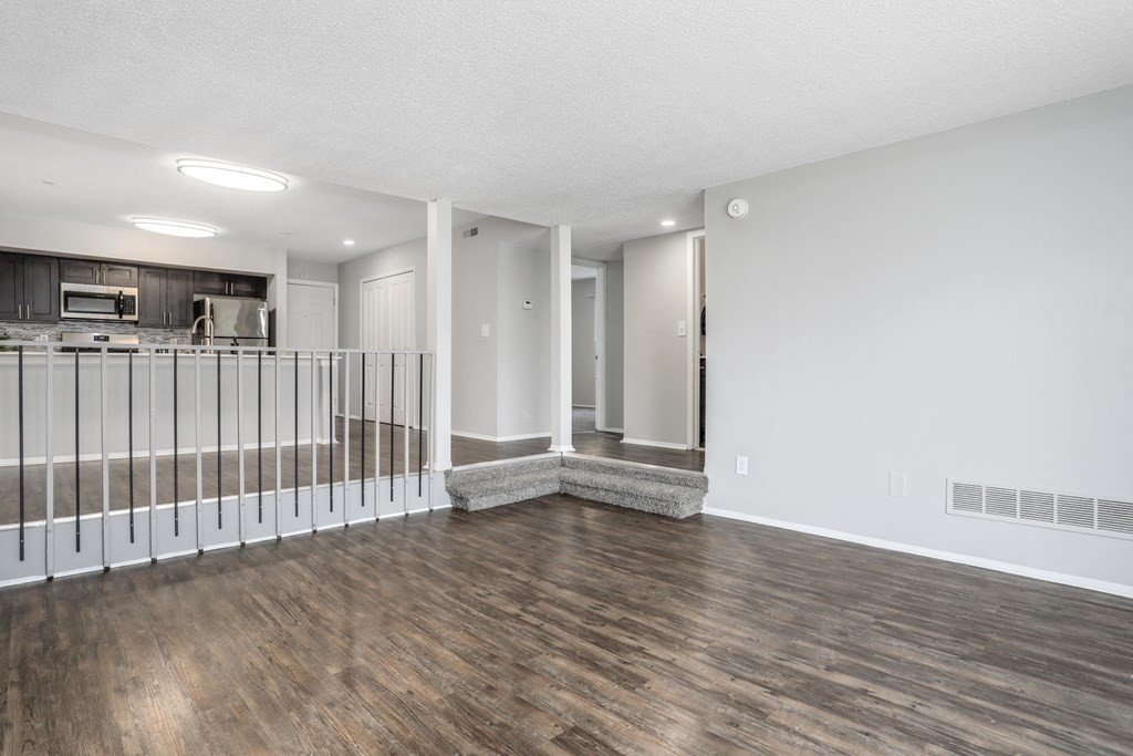 the living room and kitchen of a renovated apartment with wood flooring and a railing