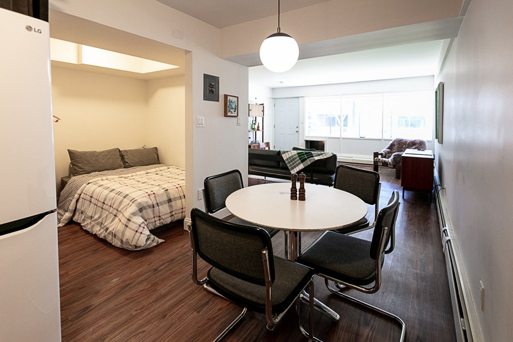 a dining area with a table and chairs and a bed in the background