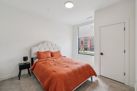 A bedroom with a bed covered in an orange comforter.