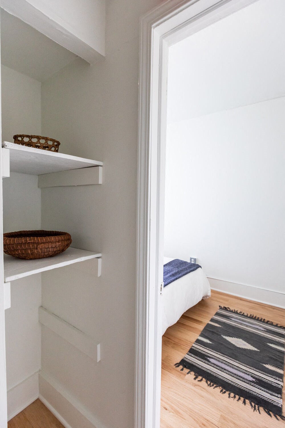 a bedroom with white walls and a white bed with a blue blanket and a rug on the