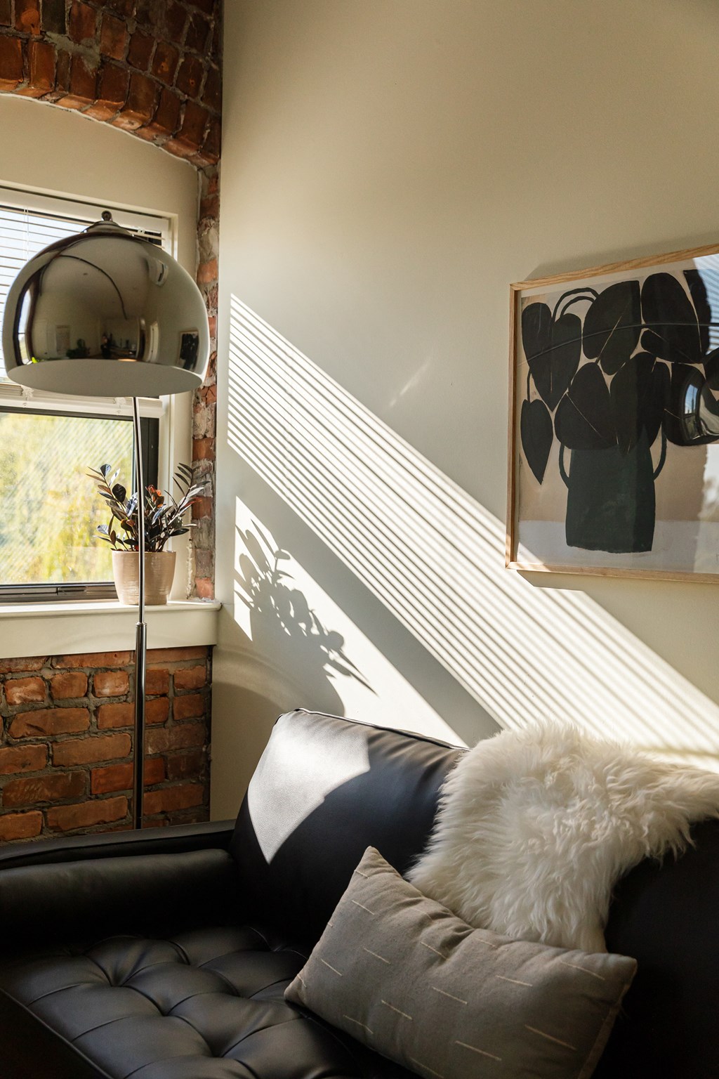 a corner of a room with a black leather couch and a white fur pillow