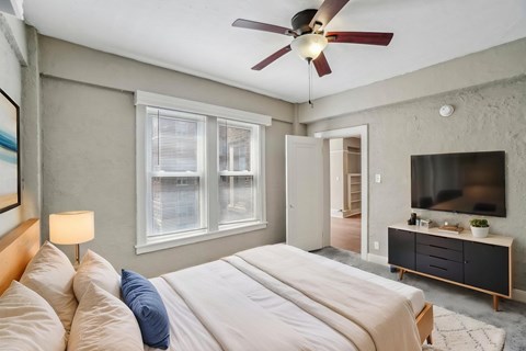 A bedroom with a bed, a ceiling fan, and a television.