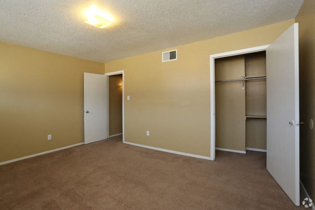 Bedroom with tan carpeting and tan walls with a closet and extensive shelving.