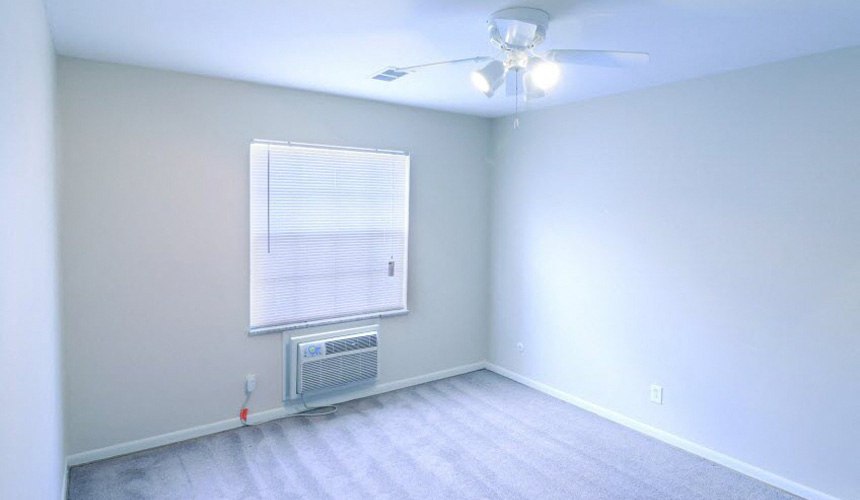 Bedroom with white walls, grey carpet, a ceiling fan, large window, and AC unit.