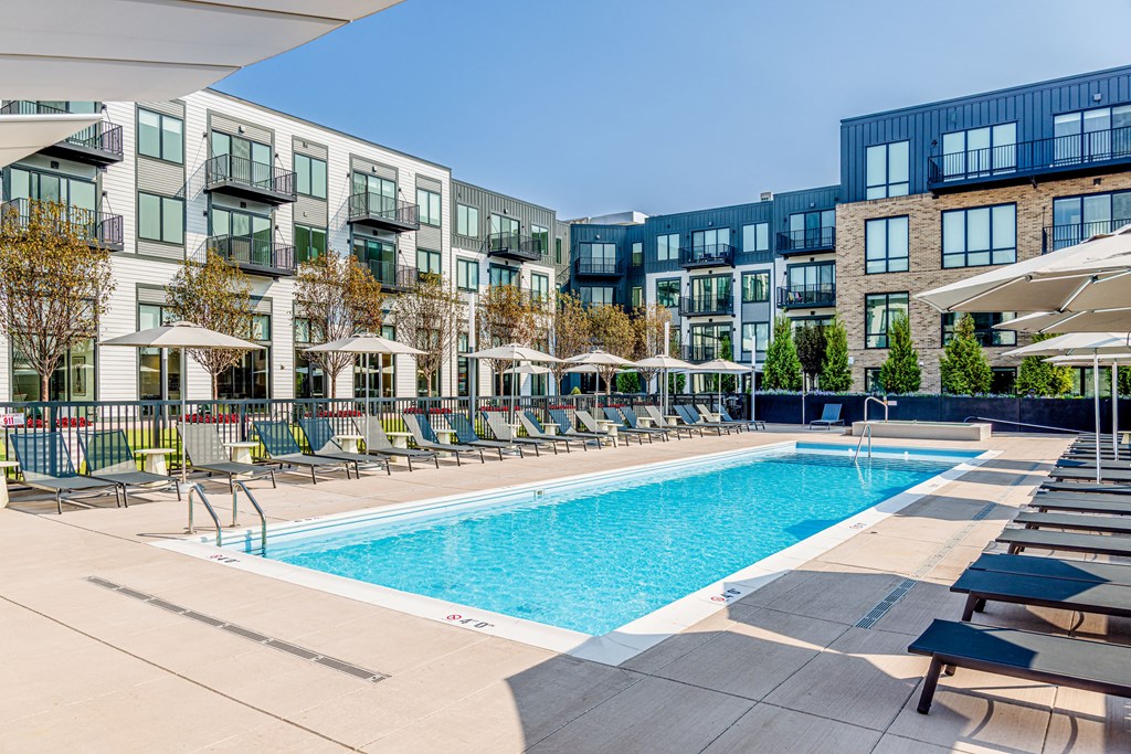 a swimming pool with chairs and umbrellas in front of apartment buildings
