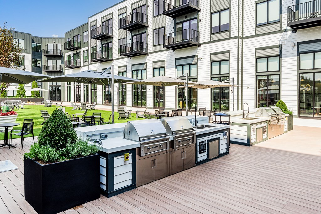 an outdoor patio with barbecue grills and umbrellas in front of a building