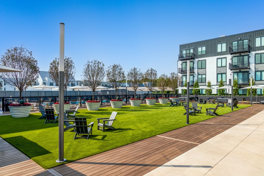 a grassy area with benches and chairs in front of an apartment building
