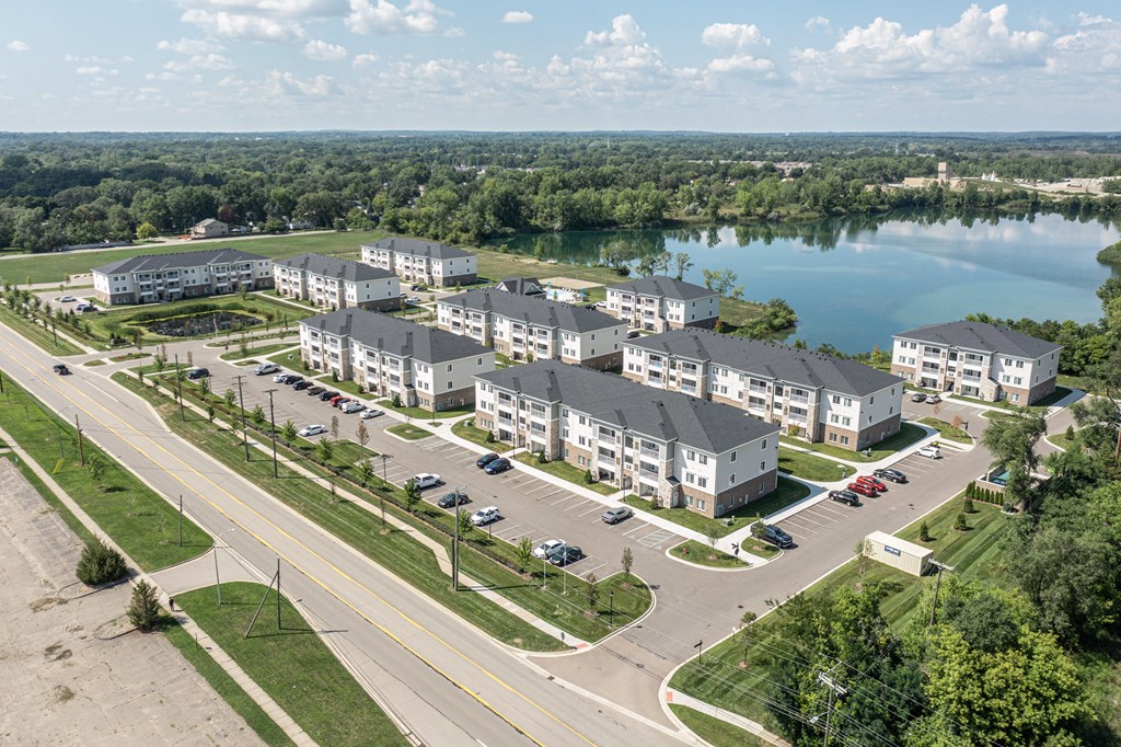 Sky view of the community with large pond behind community. Green grass and paved roads throughout.
