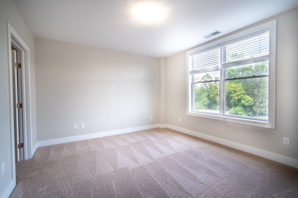 Bedroom with plush carpeting, cream walls, and a large picture window.