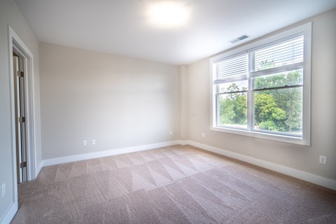 Bedroom with plush carpeting, cream walls, and a large picture window.