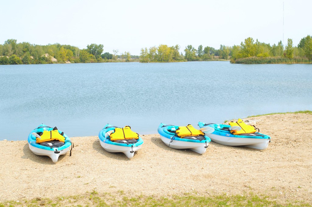 Lake with sand beach. On the beach there are four kayaks. All of the kayaks are blue with yellow life vests on them.