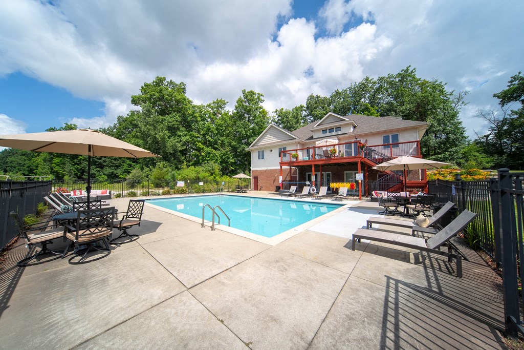 a swimming pool with chairs and umbrellas in front of a house