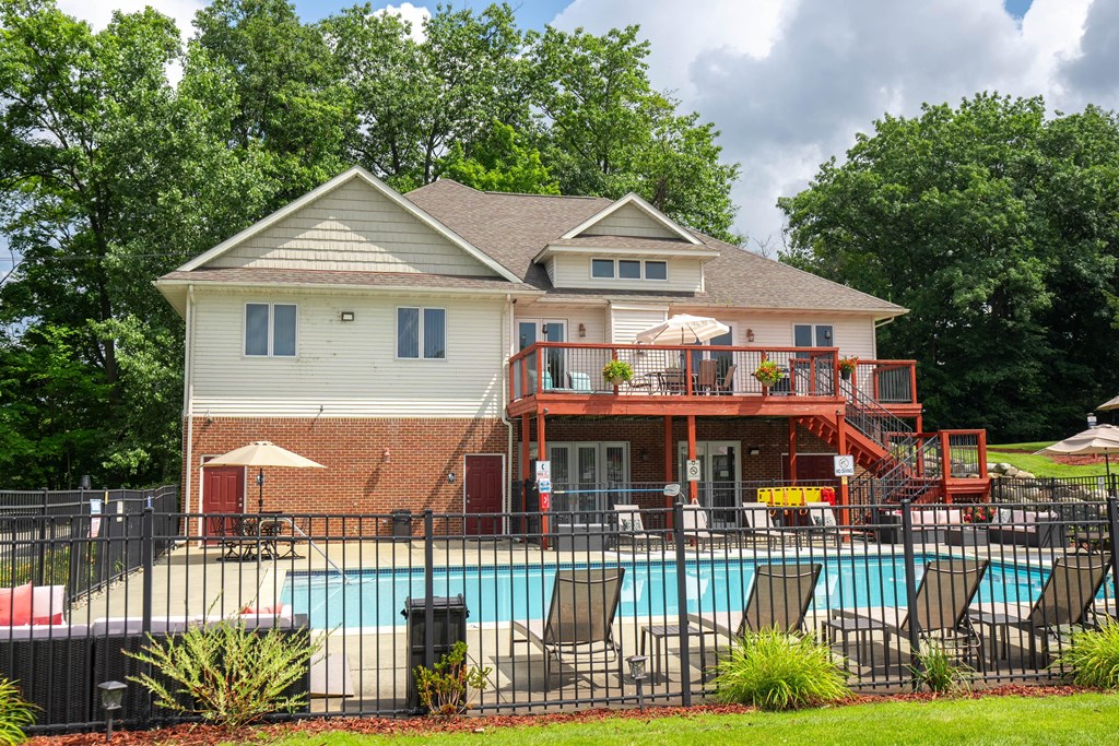 a swimming pool in front of a house with a deck with chairs