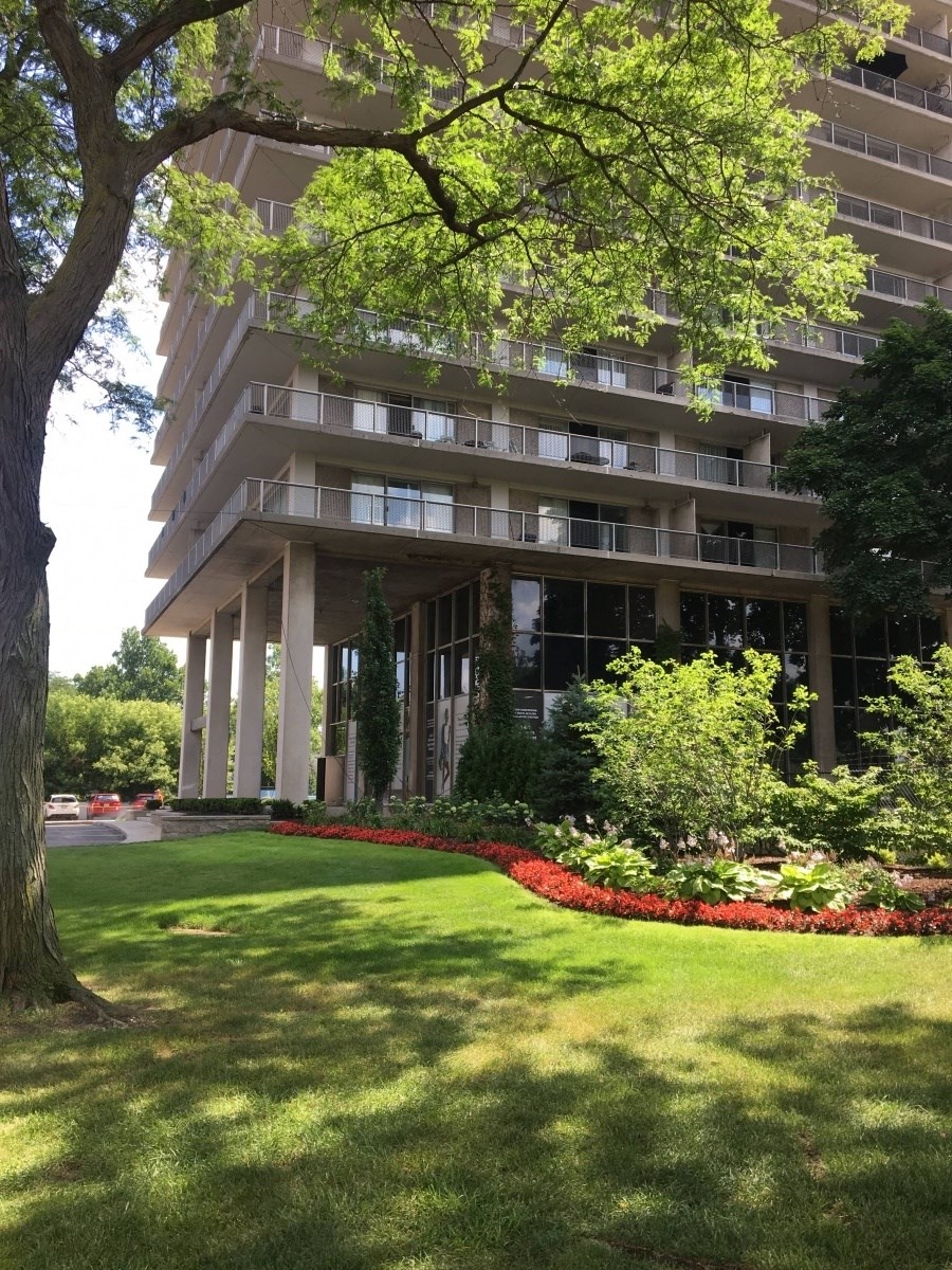 Exterior of The Jefferson. There is green grass with red flowers around the monument sign. The image shows the main enterance to the building. There is a large tree in the photo.