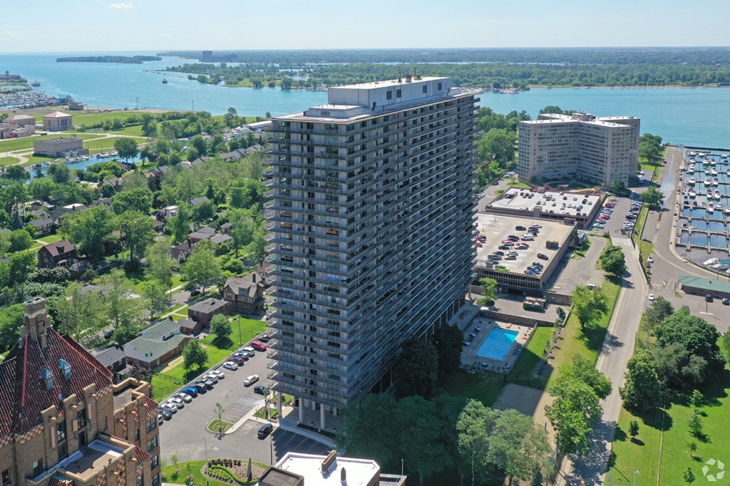Exterior of the Jefferson. The building stands 30 stories tall. The building is located on the Detroit River. There are green trees and roadways around the building.