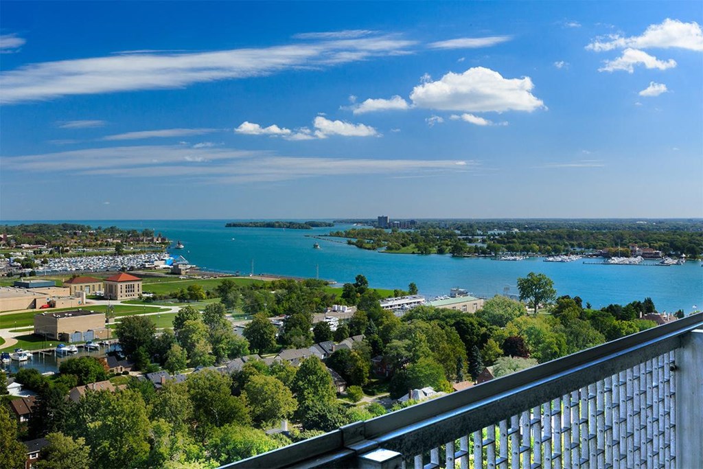 View from The Jefferson. The building is on the Detroit River. There are green trees and a blue sky. The water is a bright blue.