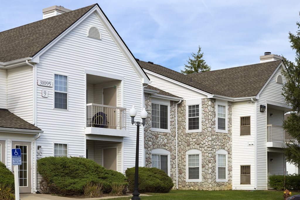 A white building with a stone wall and a blue sign with a white wheelchair symbol.