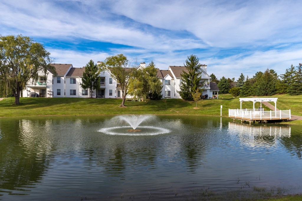 a fountain in the middle of a pond with apartments in the background at Village Club of Farmington Hills, Farmington Hills, MI 48331
