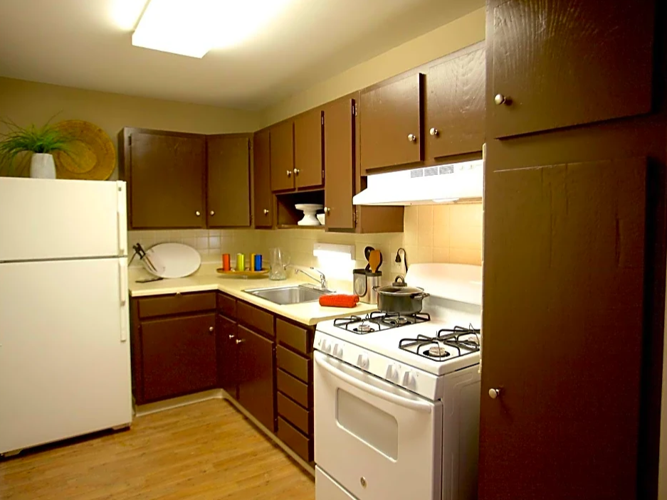Kitchen with dark cabinetry, white appliances and 2-tone beige paint.  White ceiling with rectangle light.  Light wood flooring.