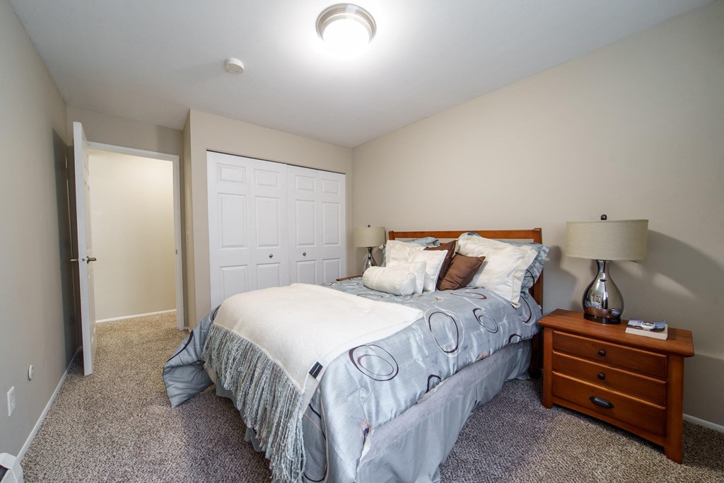 Second Bedroom With Closet Storage Bedroom with plush carpeting, bed with blue bedding, and wooded nightstand with lamp on top and a large white closet.