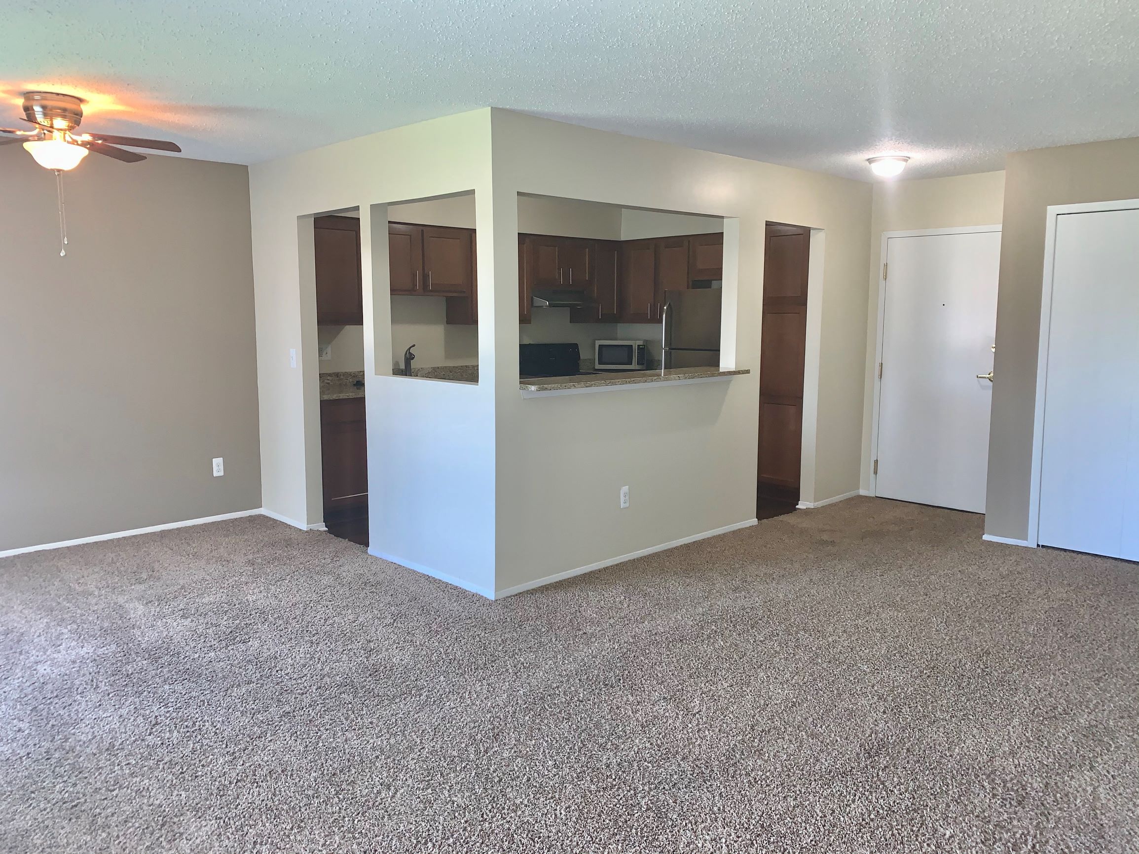 an empty living room with a kitchen and a ceiling fan
