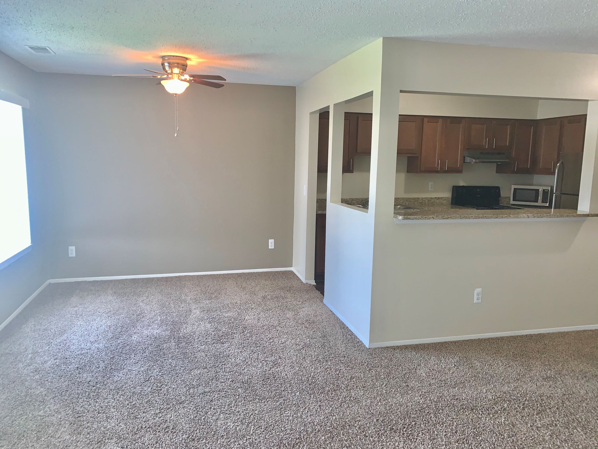 an empty living room and kitchen with a ceiling fan