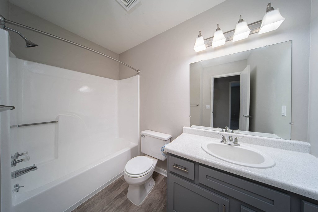 modern bathroom with tub, sink, toilet, mirror, and light