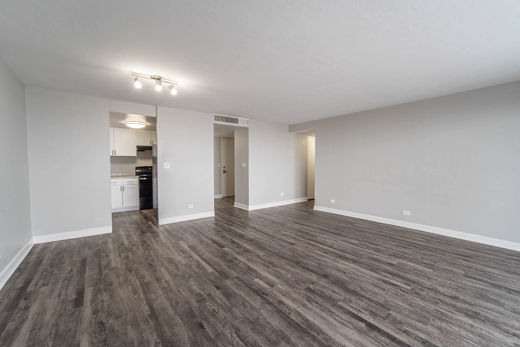 an empty living room with wood flooring and a kitchen