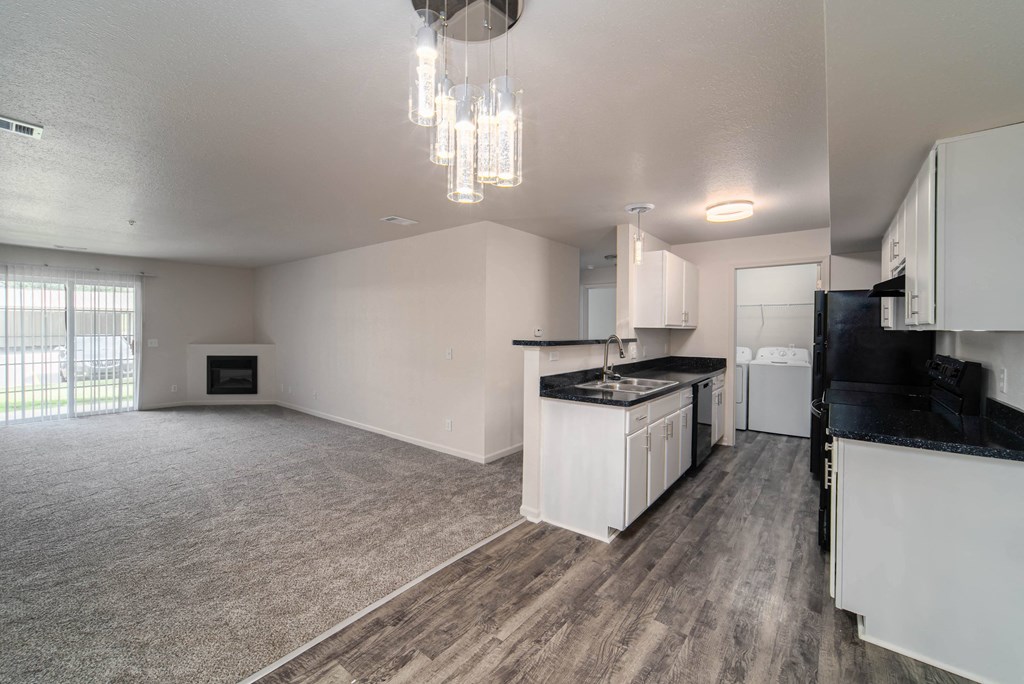 an empty living room and kitchen with white cabinets and black counter tops