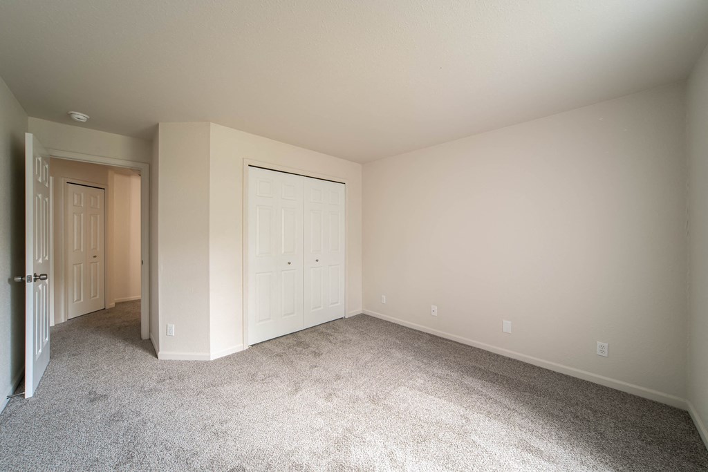 a bedroom with white walls and carpet and a door to a closet