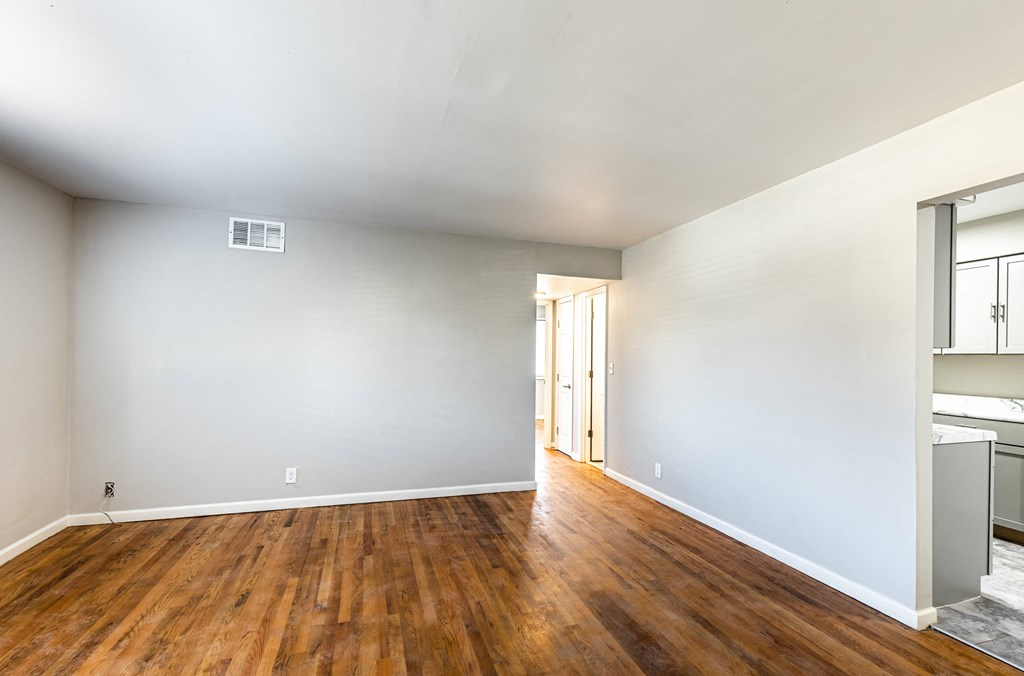 the living room and dining room of an apartment with wood floors and white walls