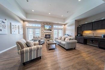 Inside clubhouse, high ceilings, striped grey furniture, fireplace and TV along back wall, windows on the left and right side of frireplace. - Photo Gallery 16