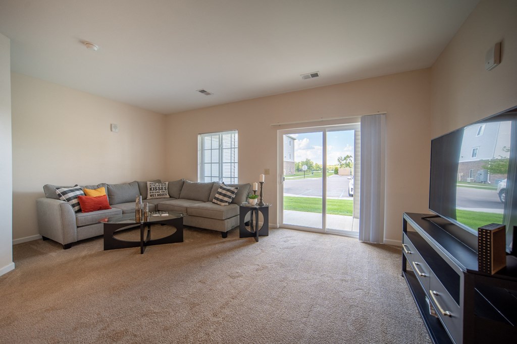 Image of living room, door leading to patio on the right, light tan painted walls, grey couch in left corner of room with coffee table in front.