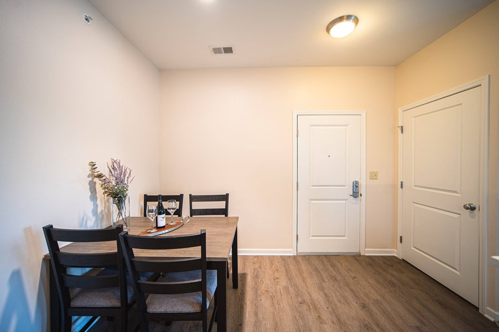 Dining room with table against wall, wine glasses on table, door on the right side of room.