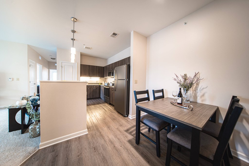 Dininig room leading into kitchen, grey wood like floors, dining table on right, walway leading to kitchen, living room on left.