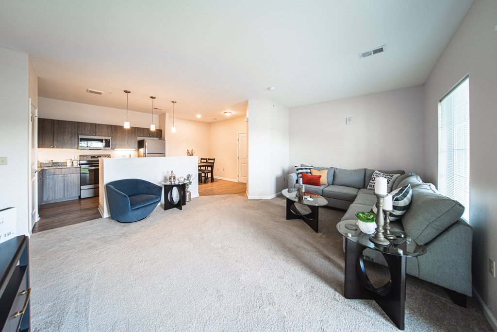 Living room leading into kitchen, blue chair next to island countertop, couch to the right in the corner, light tan carpet.