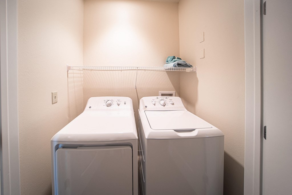 Side by side full sized washer and dryer inside of a closet, rack above washer and dryer.