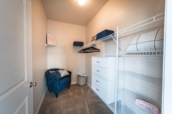 Image of walk in closet, tall ceilings, shelving on the right with hangers, chair in left corner. White shelving. - Photo Gallery 10