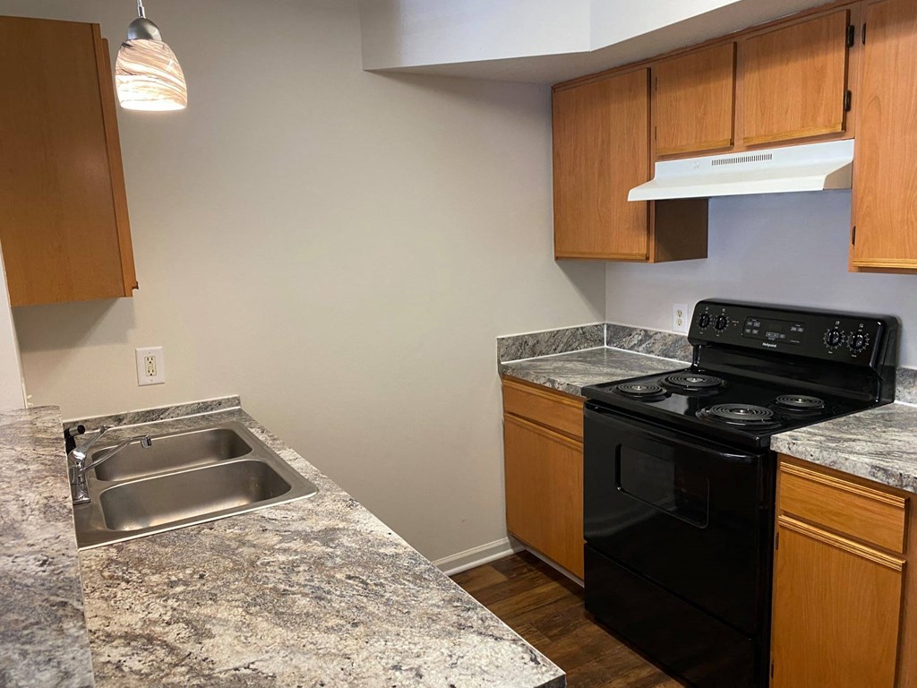 Kitchen with a balck stove, stainless steel sink, wood cabients, and hardwood-like flooring.