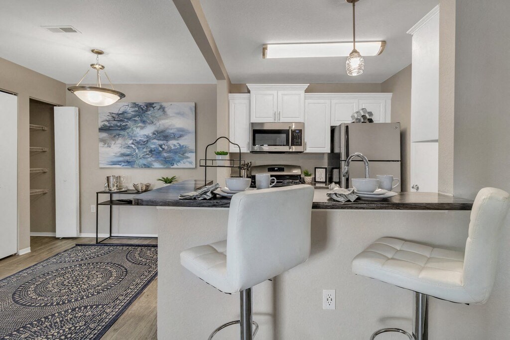 an open kitchen and living room with a bar and white chairs
