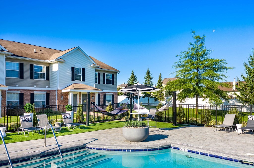 a swimming pool with chairs and umbrellas in front of a house