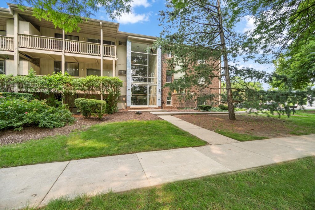 a sidewalk in front of an apartment building with grass and trees